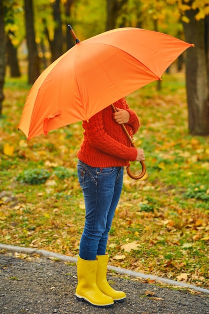 Funny unrecognizable kid under an orange umbrella