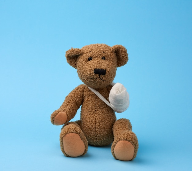 Funny vintage brown curly teddy bear with rewound paw with white gauze bandage