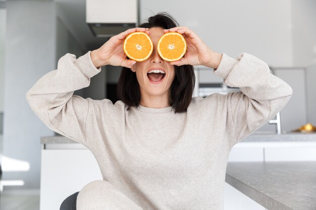  funny woman 30s holding two pieces of orange, while sitting in living room