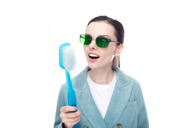 funny woman in green glasses holds a big toothbrush in her hand white background