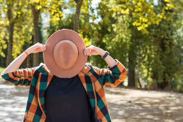 Funny Woman Hiding Her Face With A Hat In A City Park.