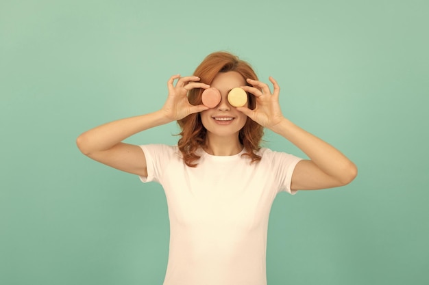 Funny woman hold sweet macaron french cookie on blue background