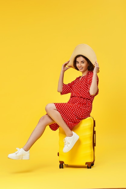 Funny woman in red dress with suitcase going traveling on yellow background.