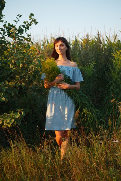 Funny woman in sky blue dress with bouquet of field flowers in sunset