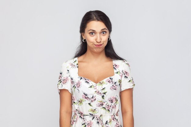 Photo funny woman wearing white dress standing looking at camera frowning face trying not to laugh