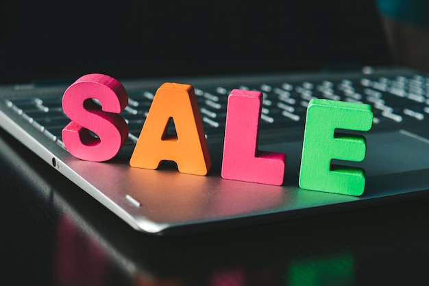 Funny word Sale set on notebook bottom. Colorful sign Sale on black surface at black screen background. Shopping online concept. Internet marketing. E-commerce. Wooden letters promote e-shopping.