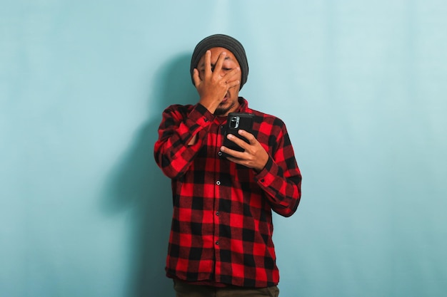 Funny Young Asian man is peeking at inappropriate content on his phone isolated on blue background