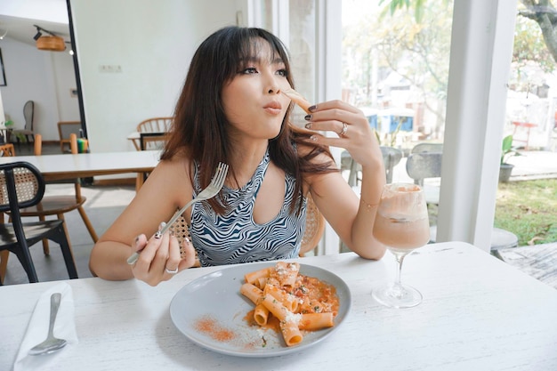 Funny young Asian woman eating tasty pasta in cafe