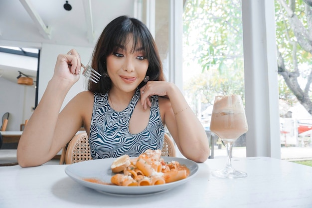 Funny young Asian woman eating tasty pasta in cafe