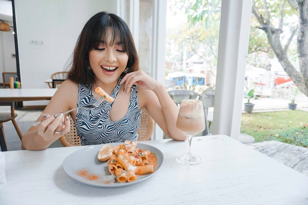 Funny young Asian woman eating tasty pasta in cafe