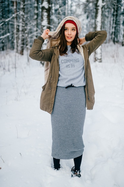 Funny young attractive brunette girl making a turban from the scarf posing in the snow forest