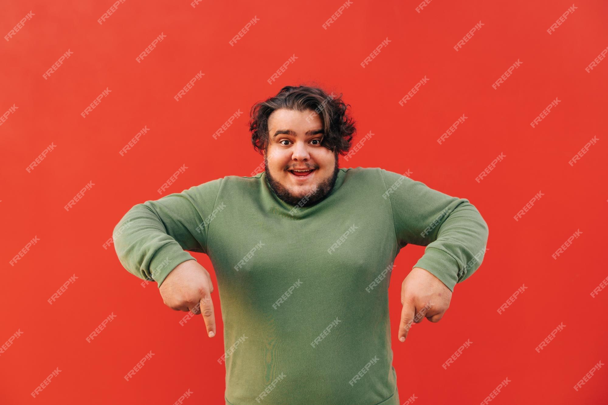 Premium Photo | And funny young bearded fat guy is standing on a red background and pointing his fingers down Premium Photo | And funny young bearded fat guy is standing on a red background and pointing his fingers down