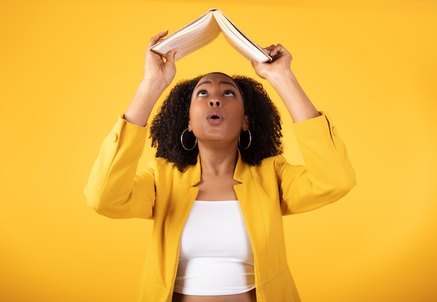 Photo funny young black lady student lifting book up and reading searching info isolated on yellow