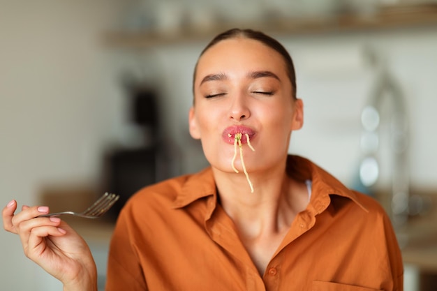 Foto divertente giovane signora caucasica che assaggia spaghetti fatti in casa che si godono il pasto di pasta con gli occhi chiusi seduti