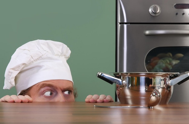 Funny young chef strange looking at pot