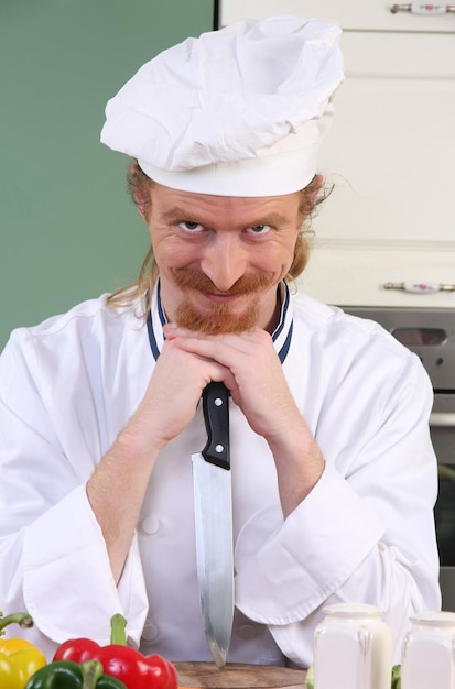 Funny young chef with a knife in kitchen