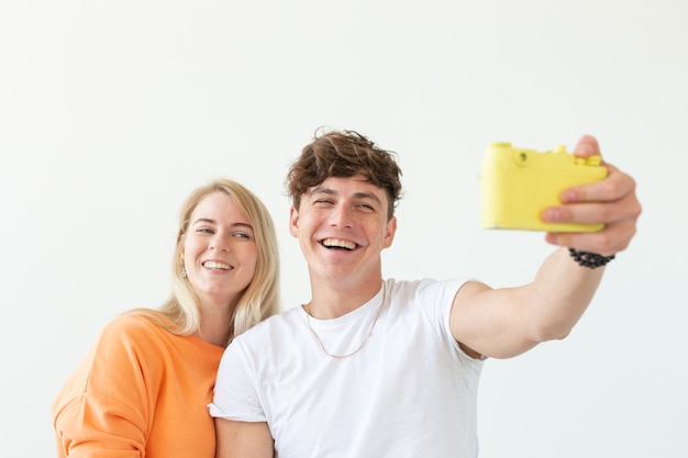 Funny young couple in love cute man and charming woman making selfie on vintage yellow film camera