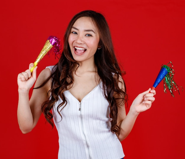 Funny young and cure Asian girl holding and playing party popers with funny and happy. Studio shot on red background.