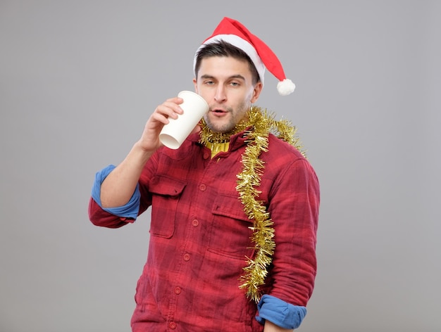 Funny young drunk man wearing Santa hat holding a paper cup