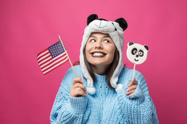 Funny young girl standing with yummy pandalollipop in her hand and a hat on his head on a pink