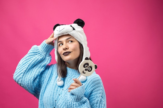 Ragazza divertente in piedi con un delizioso pandalollipop in mano e un cappello in testa