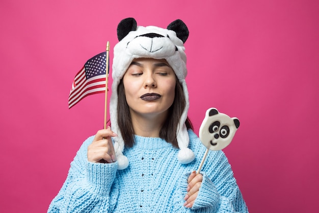 Funny young girl standing with yummy pandalollipop in her hand and a hat on his head