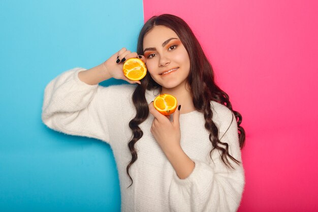 Ragazza divertente in abiti estivi che coprono gli occhi con metà di frutta fresca e matura di pompelmo arancione isolata su sfondo rosa pastello. lo stile di vita vivido della gente si rilassa il concetto di vacanza. mock up copia spazio