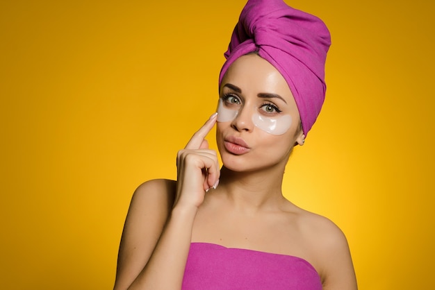 Funny young girl with a pink towel on her head pasted patches under her eyes