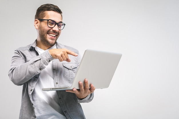 Giovane uomo bello divertente in computer portatile della tenuta della camicia e sorridere mentre stando contro il fondo bianco. divertiti.