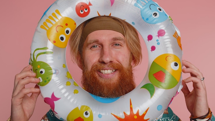 Photo funny young hippie tourist man looking out of rubber swimming ring summer vacation time sea travel