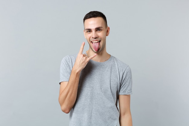 Funny young man in casual clothes showing tongue, depicting heavy metal rock sign gesture 