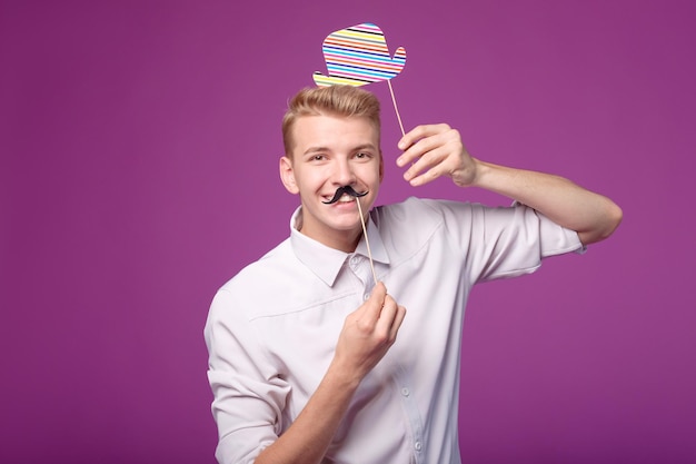 Photo funny young man with paper mustache and hat on background