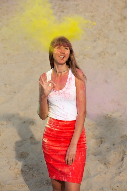 Funny young model wearing white t shirt, enjoying Holi festival at the desert, showing ok gesture