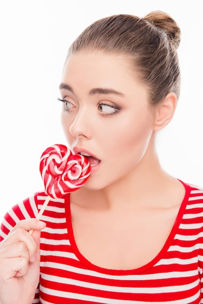 Смешная молодая красивая девушка ест красный леденец на палочке