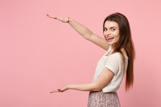 Funny young woman in casual light clothes posing isolated on pink wall background, studio portrait. People lifestyle concept. Mock up copy space. Gesturing demonstrating size with vertical workspace.