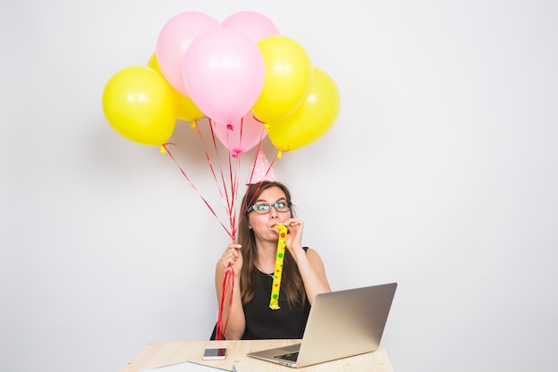 Funny young woman celebrating the success of her business or a birthday in the office holding colorful party balloons.