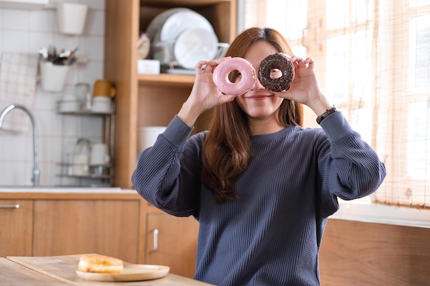 面白い若い女性が彼女の目を覆い、ドーナツの穴を通して見ています