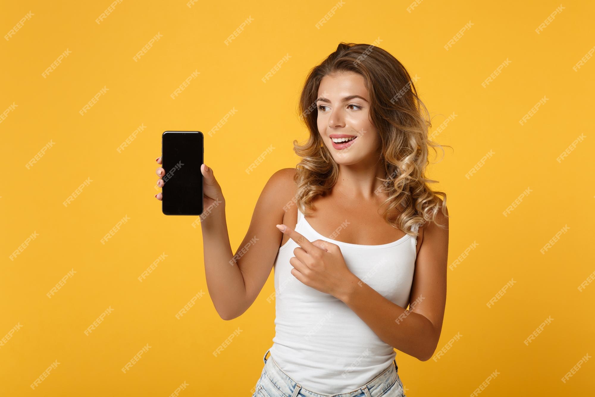 Premium Photo | Funny young woman girl in light casual clothes posing isolated on yellow orange background. people lifestyle concept. mock up copy space. pointing index finger on mobile phone with blank Premium Photo | Funny young woman girl in light casual clothes posing isolated on yellow orange background. people lifestyle concept. mock up copy space. pointing index finger on mobile phone with blank