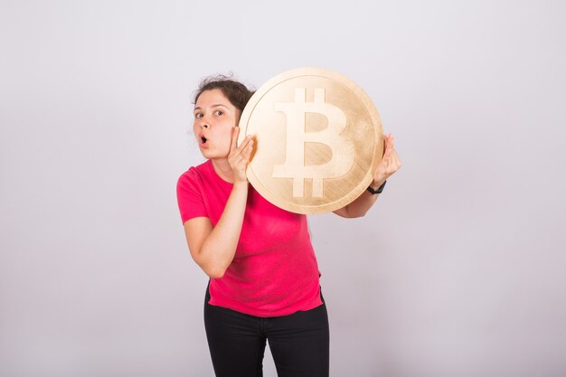 Funny young woman holding big bitcoin on white space