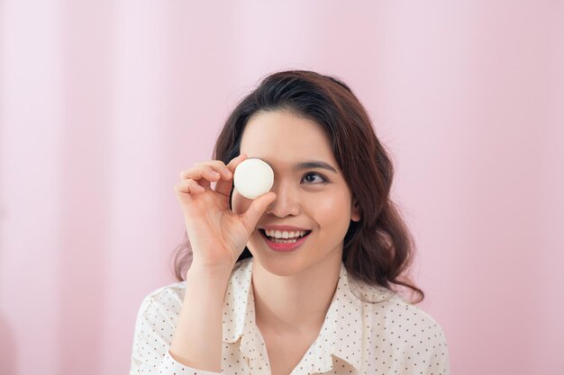 분홍색 배경에 눈 근처에 마카롱을 들고 있는 재미있는 젊은 여성