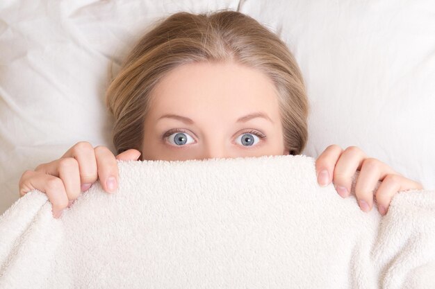 Фото Смешная молодая женщина лежит в постели под одеялом