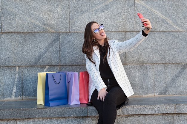 Funny young woman makes selfie on the street with her shopping bags