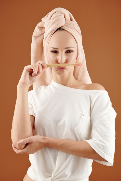 Funny young woman posing with woden toothbrush after taking shower