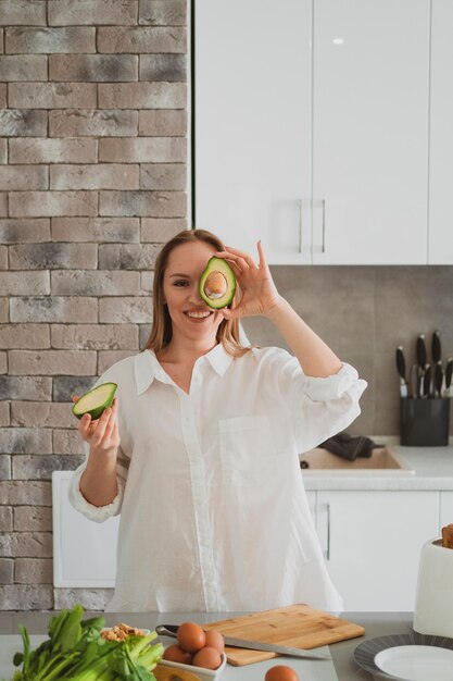 Divertente giovane donna che mostra fette di avocado in cucina