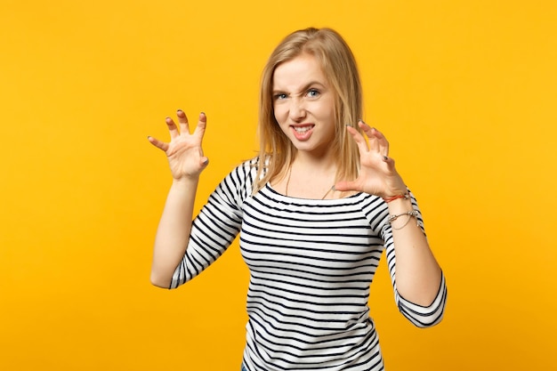 Funny young woman in striped clothes shouting, growling like animal, making cat claws gesture isolated on yellow orange wall background. People sincere emotions, lifestyle concept. Mock up copy space.