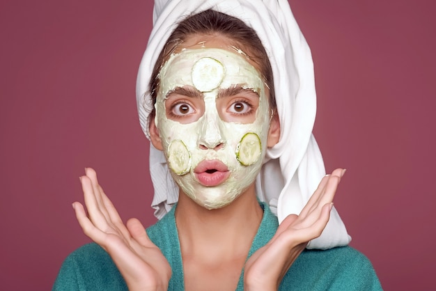 Giovane donna divertente con maschera di cetriolo sul viso. ringiovanimento, salute, giovinezza. concetto di salone di bellezza. cura della pelle e dei capelli, spa, benessere. ragazza con telo da bagno sulla testa.