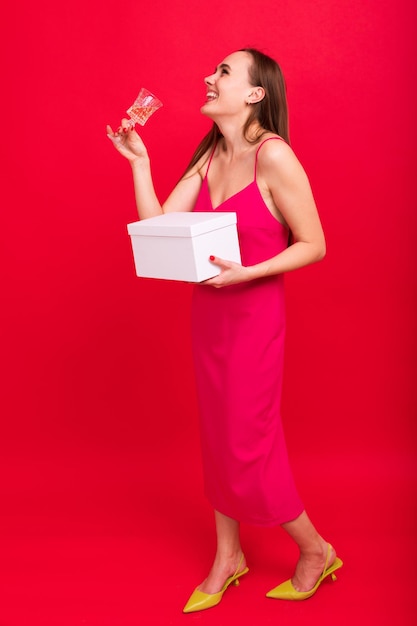 Funny young woman with a glass of champagne and a gift for the New Year on a red background