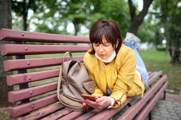 面白い若い女性は、保護マスクと公園のベンチで彼女の胃の上に横たわっています