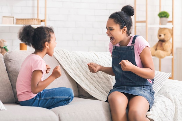 Furious african sisters screaming at each other on couch