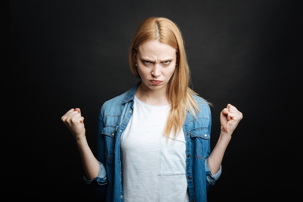 Photo furious irritated young woman expressing rage and showing fists while looking with anger and standing against black wall